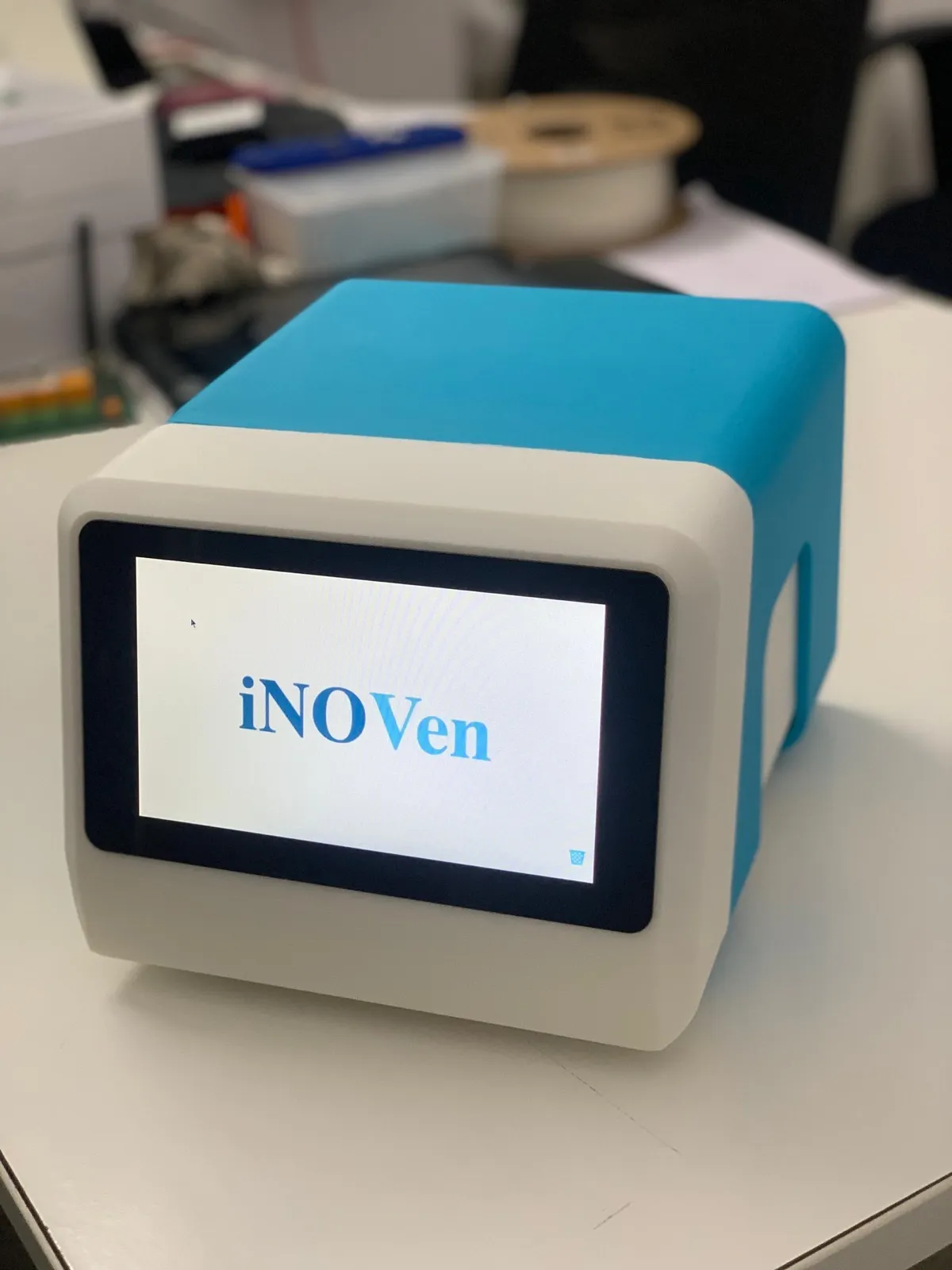 The iNO-VEN inhaled nitric oxide prototype on a workbench, showing its 7-inch touchscreen on the cyan and grey housing